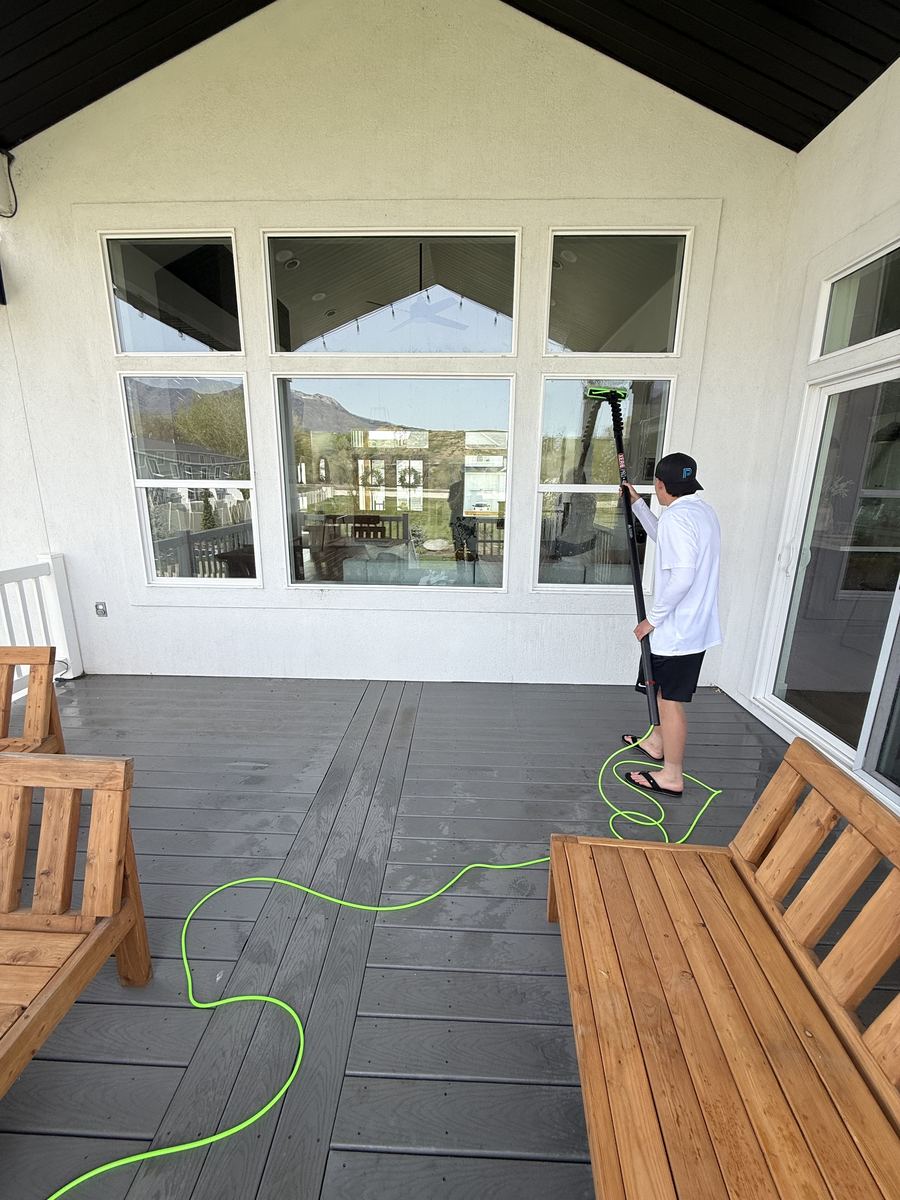 Cleaning large windows on a grey home with covered outdoor living space